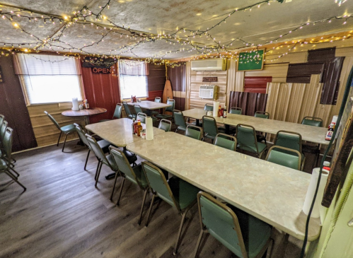 A cozy dining room with tables, chairs, and string lights, featuring a welcoming "OPEN" sign.