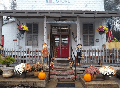 A charming storefront with scarecrows, colorful flowers, pumpkins, and a welcoming red door.