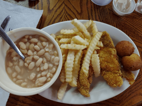 A plate with crinkle-cut fries, fried fish fillets, cornbread muffins, and a bowl of white beans.