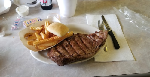 A plate with a grilled steak, crinkle-cut fries, and a bun, accompanied by a knife and fork on a table.