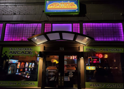 A brightly lit arcade entrance featuring neon signs, pinball machines, and a welcoming atmosphere.