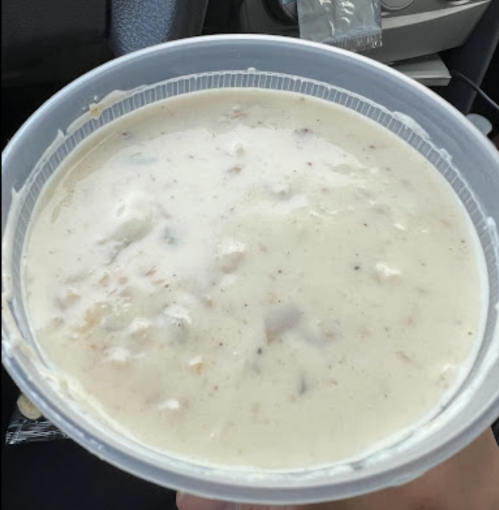 A person holding a large container of creamy soup or chowder, with a thick, textured consistency.