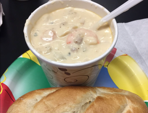 A cup of creamy seafood chowder with shrimp, served with a piece of bread on a colorful paper plate.