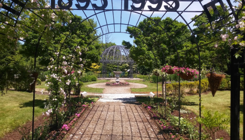 A garden path leads to a gazebo, framed by blooming flowers and greenery under a clear blue sky.