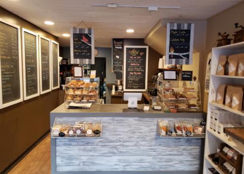 Cozy café interior with a counter displaying baked goods and coffee options, chalkboard menus on the walls.