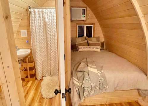 Cozy wooden interior of a small cabin featuring a bed, seating area, and a bathroom with a shower curtain.