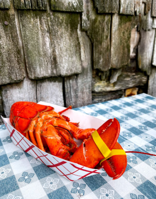 A cooked lobster in a paper tray on a checkered tablecloth, with a rustic wooden background.