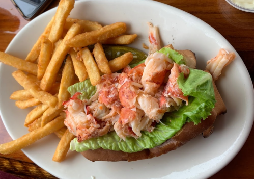 A lobster roll topped with lettuce, served with a side of golden French fries on a white plate.
