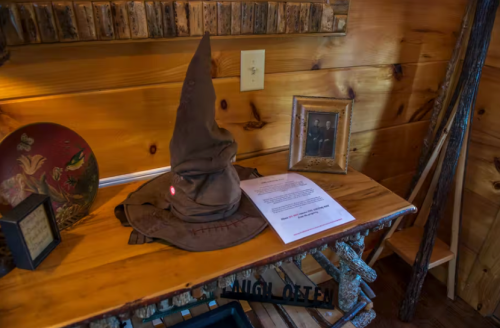 A brown, pointed hat sits on a wooden table next to a framed photo and a piece of paper in a rustic setting.