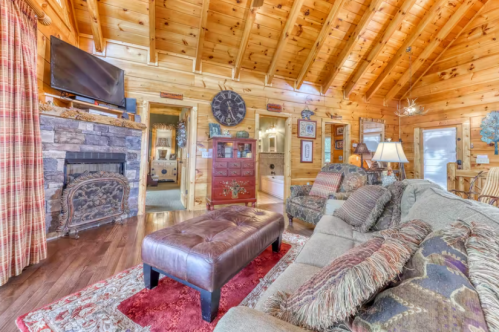 Cozy log cabin living room with wooden beams, a stone fireplace, and comfortable seating. Warm, inviting atmosphere.