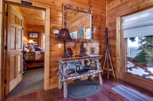 Cozy wooden entryway with a rustic mirror, table, and door leading to a bedroom, featuring warm lighting and decor.