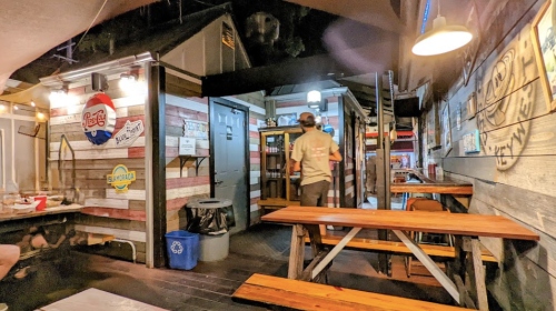 A person walks through a rustic restaurant with wooden tables and walls adorned with signs and artwork.