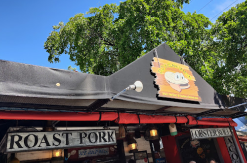 A colorful restaurant sign reading "Porky's" above a food stall with signs for roast pork and lobster rolls.