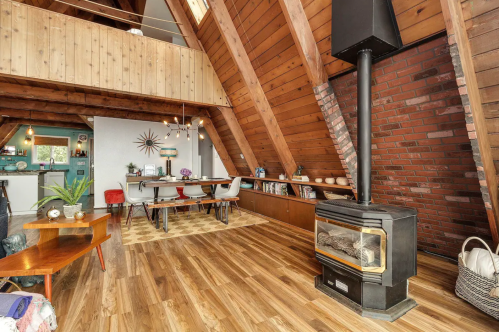 Cozy A-frame interior with wooden beams, a fireplace, dining area, and modern decor. Warm, inviting atmosphere.