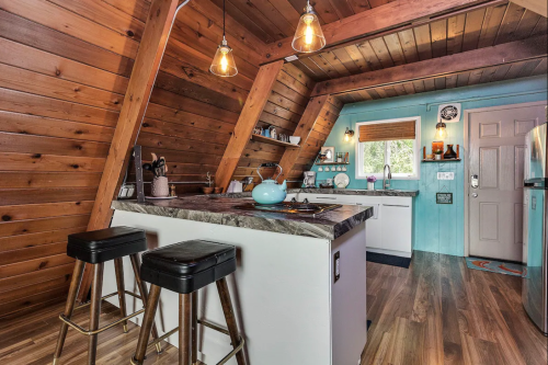 Cozy kitchen with wooden walls, modern appliances, and a small island with bar stools, featuring warm lighting.