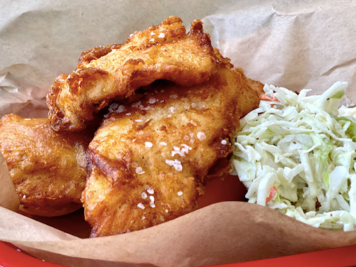 Crispy fried fish fillets with a side of coleslaw, served in a paper-lined basket.