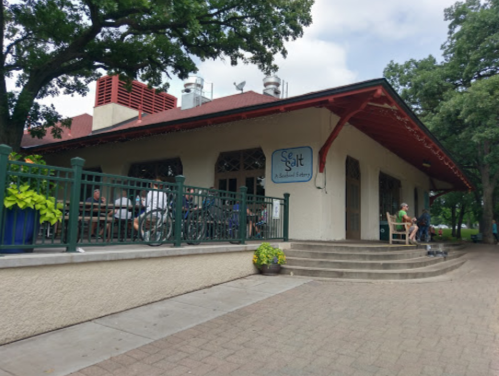 A café with outdoor seating, surrounded by trees, featuring a sign that reads "Salt" and people enjoying their time.