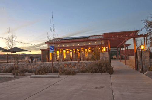A modern building with a wooden facade, surrounded by landscaping, under a colorful sunset sky.