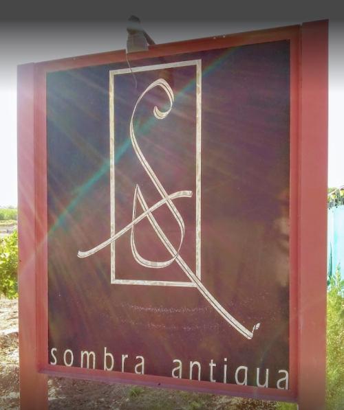 Sign for "Sombra Antigua" featuring a stylized logo and a dark background, illuminated by sunlight.