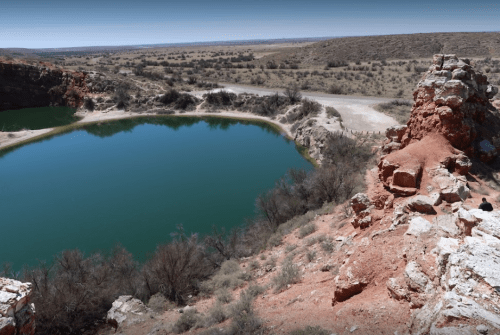 A serene pond surrounded by rocky terrain and sparse vegetation under a clear blue sky.
