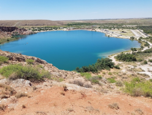 A serene blue lake surrounded by rocky terrain and sparse greenery under a clear sky.