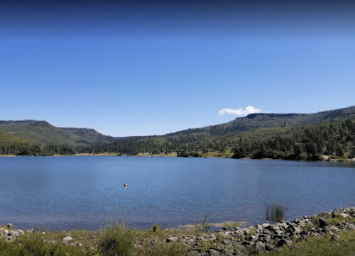 A serene lake surrounded by green hills and blue skies, with a few clouds in the distance.