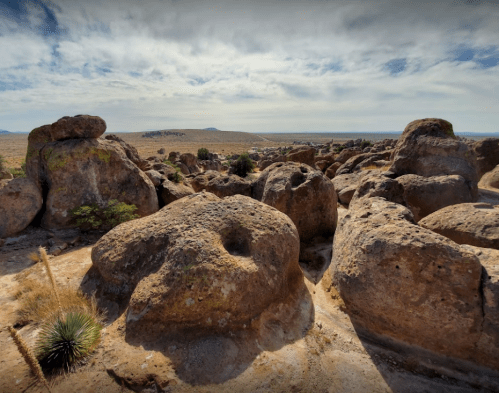 Rocky landscape with large boulders and sparse vegetation under a cloudy sky.
