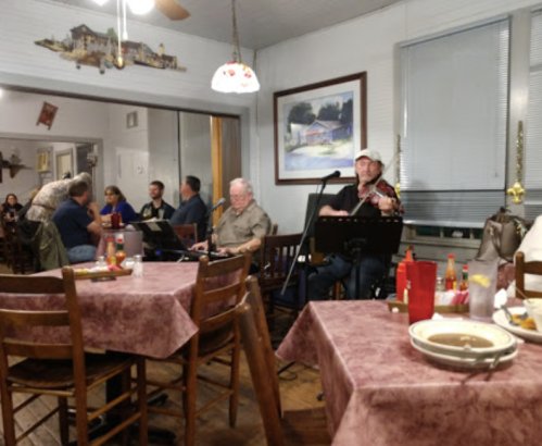 A cozy restaurant scene with diners at tables, a musician playing violin, and a man at a keyboard.
