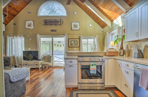Cozy cabin interior with a kitchen, living area, wooden beams, and large windows overlooking nature.
