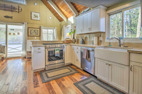 Bright kitchen with wooden floors, white cabinets, stainless steel appliances, and large windows overlooking nature.