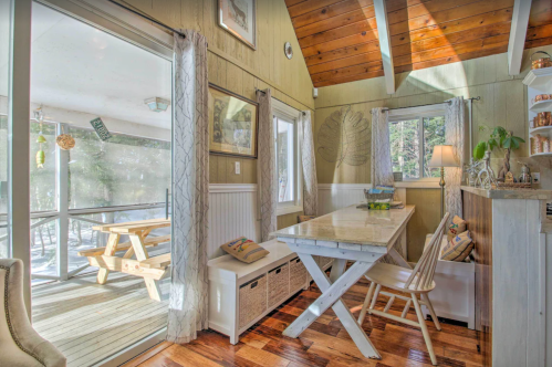 Bright, cozy dining area with a wooden table, chairs, and large windows overlooking a deck and nature.