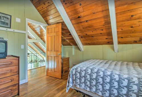 Cozy attic bedroom with wooden beams, a patterned bedspread, dresser, and a door leading to a balcony.
