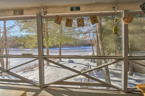 View of a snowy lake through a screened porch, with wooden letters spelling "LAKE" and trees in the background.