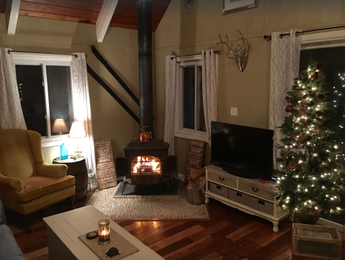 Cozy living room with a fireplace, a Christmas tree, and warm lighting, creating a festive atmosphere.