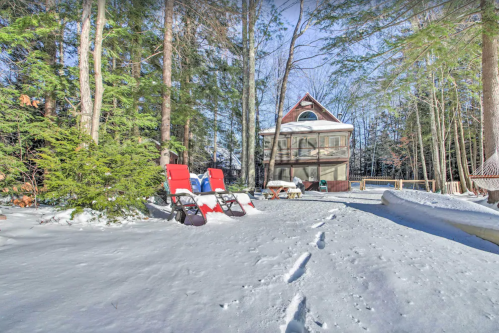 A snowy landscape with a house surrounded by trees, featuring red lounge chairs and a hammock in the foreground.