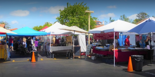 A vibrant outdoor market with colorful tents, vendors, and shoppers enjoying a sunny day.