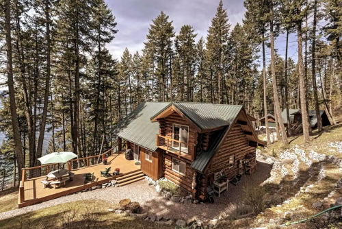 A cozy log cabin surrounded by tall trees, featuring a spacious deck and outdoor seating.