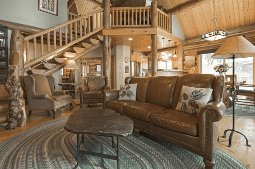Cozy log cabin interior featuring a leather sofa, rustic decor, and a wooden staircase. Warm and inviting atmosphere.
