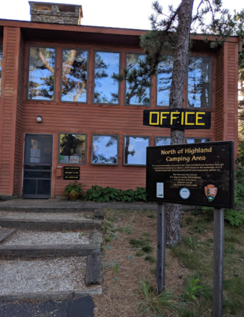 A wooden building with large windows and a sign reading "OFFICE" in front of a camping area.