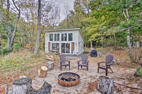 A cozy cabin surrounded by trees, with a fire pit and seating area in a serene outdoor setting.