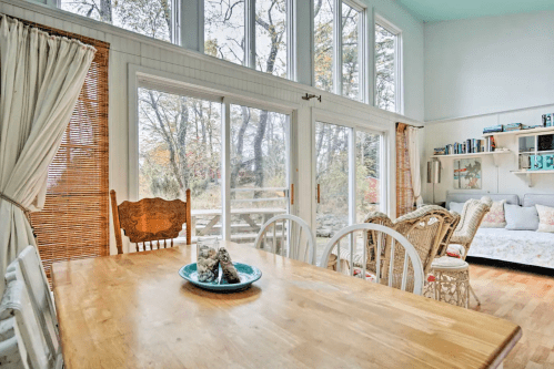 Bright, airy dining area with a wooden table, chairs, and large windows overlooking a natural landscape.