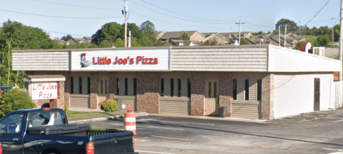 Exterior view of Little Joe's Pizza, a single-story building with a sign, surrounded by trees and parked cars.