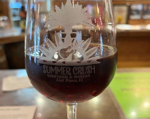A close-up of a wine glass with red wine, featuring the logo of Summer Crush Vineyard & Winery in Fort Pierce, FL.