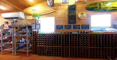 Interior of a rustic shop featuring a wine rack, shelves of products, and surfboards on the wall.