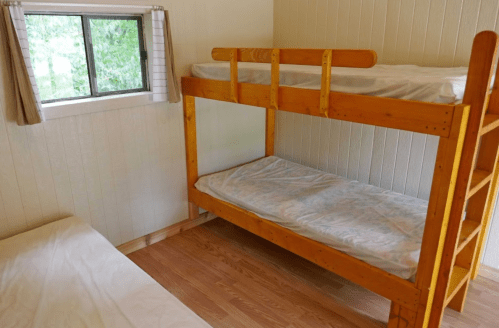 A cozy room with a wooden bunk bed and a single bed, featuring a window with natural light.