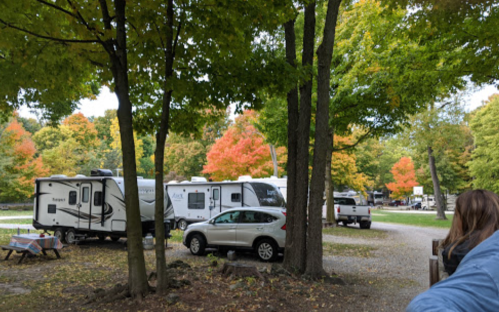 A scenic RV park with colorful autumn trees, parked RVs, and a car amidst fallen leaves.