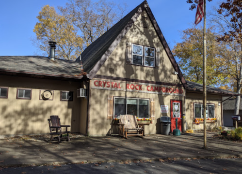 A rustic campground building with "Crystal Rock Campground" sign, surrounded by trees and outdoor seating.