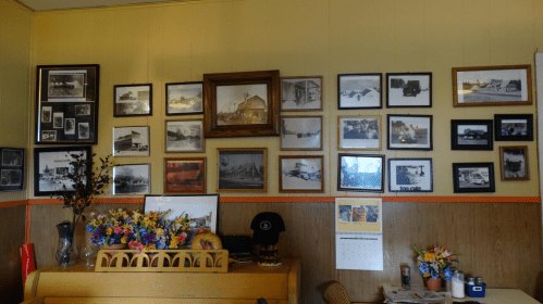 A wall adorned with framed black-and-white photos, a calendar, and colorful flower arrangements on a wooden surface.