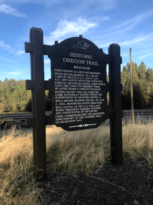 Sign marking the Historic Oregon Trail in Meacham, detailing its history and significance. Surrounded by grass and trees.