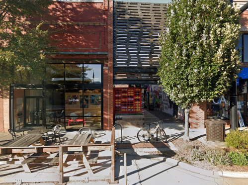 A modern building entrance with outdoor seating, trees, and colorful wall art in the background.